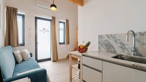 A modern kitchen with a marble countertop and a sink, a blue sofa with cushions, and a basket of fruit on a small table.