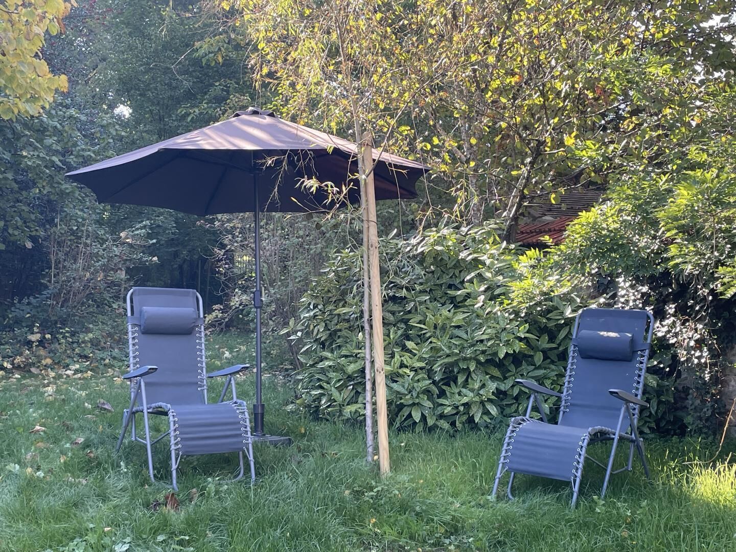 Dos sillones de relax bajo un paraguas grande en un jardín.