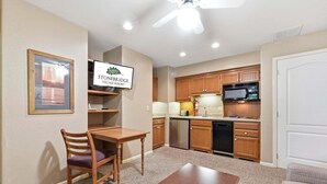 Una cocina compacta con armarios de madera, microondas y lavavajillas. Hay una mesa de comedor con sillas y un cuadro en la pared.