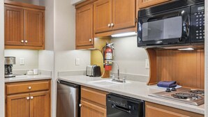 Una cocina compacta con armarios de madera, microondas, lavaplatos, tostadora y lavamanos.