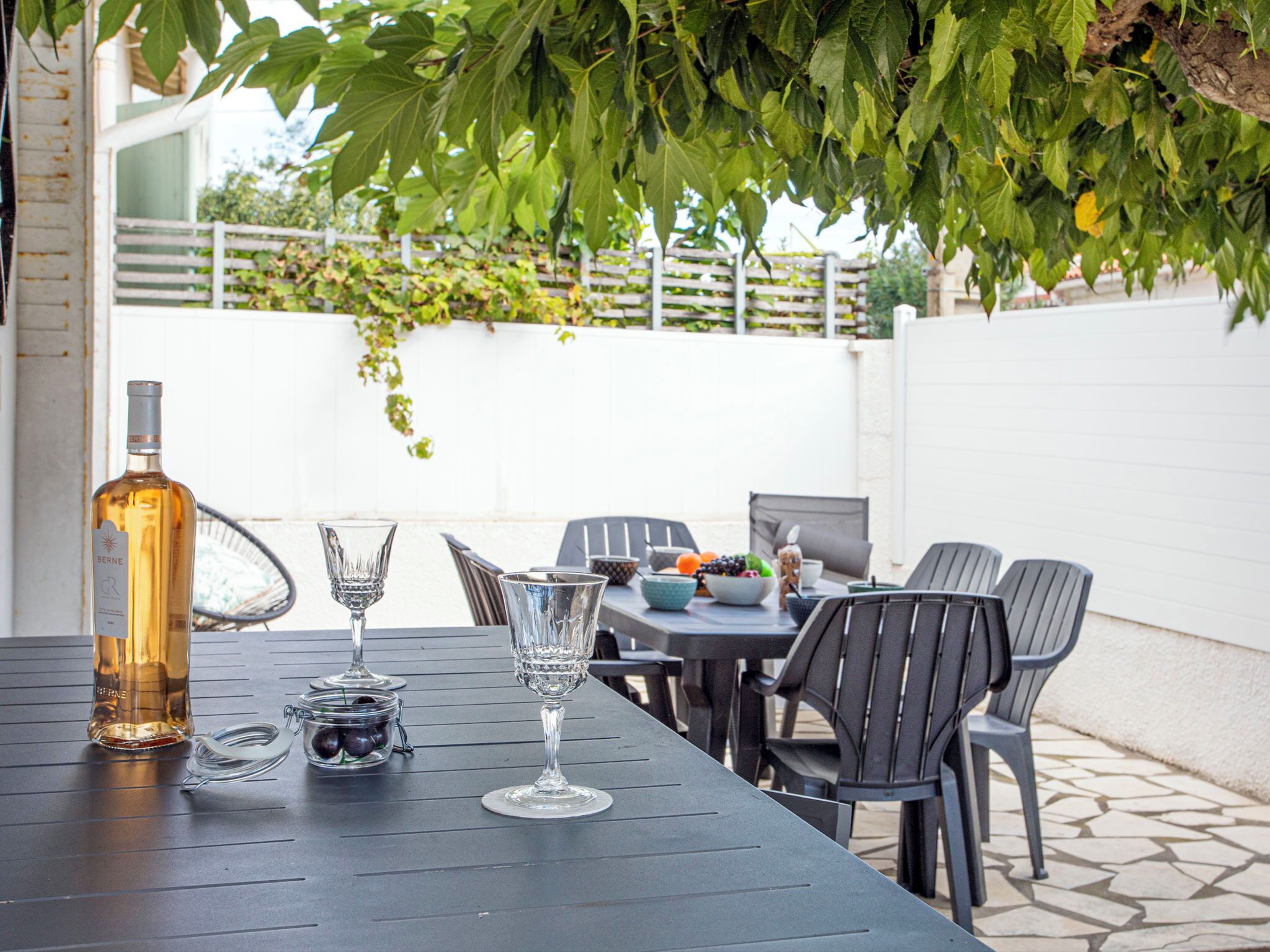 A table set outdoors with a bottle and glasses, surrounded by chairs.