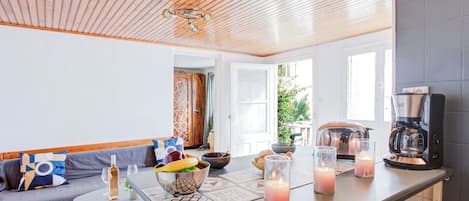 Une cuisine moderne avec un plafond en bois, une machine à café, une table à manger décorée de bougies et un coin salon confortable avec un canapé et une petite table ronde.