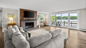 Ein geräumiges Wohnzimmer mit Kamin, einer großen Couch, einem Essbereich mit Tisch und Stühlen sowie Seeblick durch große Schiebeglastüren.