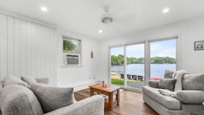 Ein modernes Wohnzimmer mit Seeblick, grauem Sofa, einem Holztisch und einem Deckenventilator.