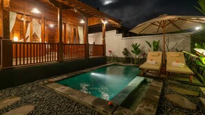 A nighttime pool area with a wooden deck, lounge chairs, and a small pool. - Pondok di Uma Villa (Tegallalang)