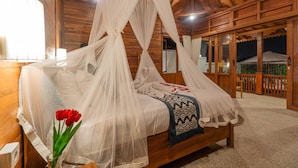 A wooden room with a bed covered in white netting, a vase with red flowers, and a patterned blanket. - Pondok di Uma Villa (Tegallalang)