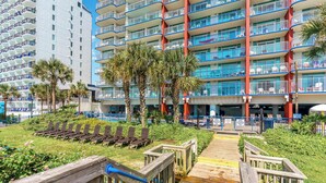A hotel with multiple balconies, a pool area with sun loungers, and a wooden boardwalk leading to the pool.