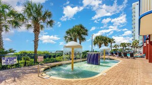 A pool area with palm trees, a no lifeguard sign, and a shallow water warning.