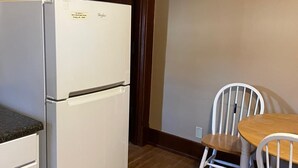 A compact kitchen with a white refrigerator, a wooden dining table with two chairs, and a wooden door. - Cozy Private Room in Historic Findlay Home with Kitchen, Wifi and Free Parking (Findlay)