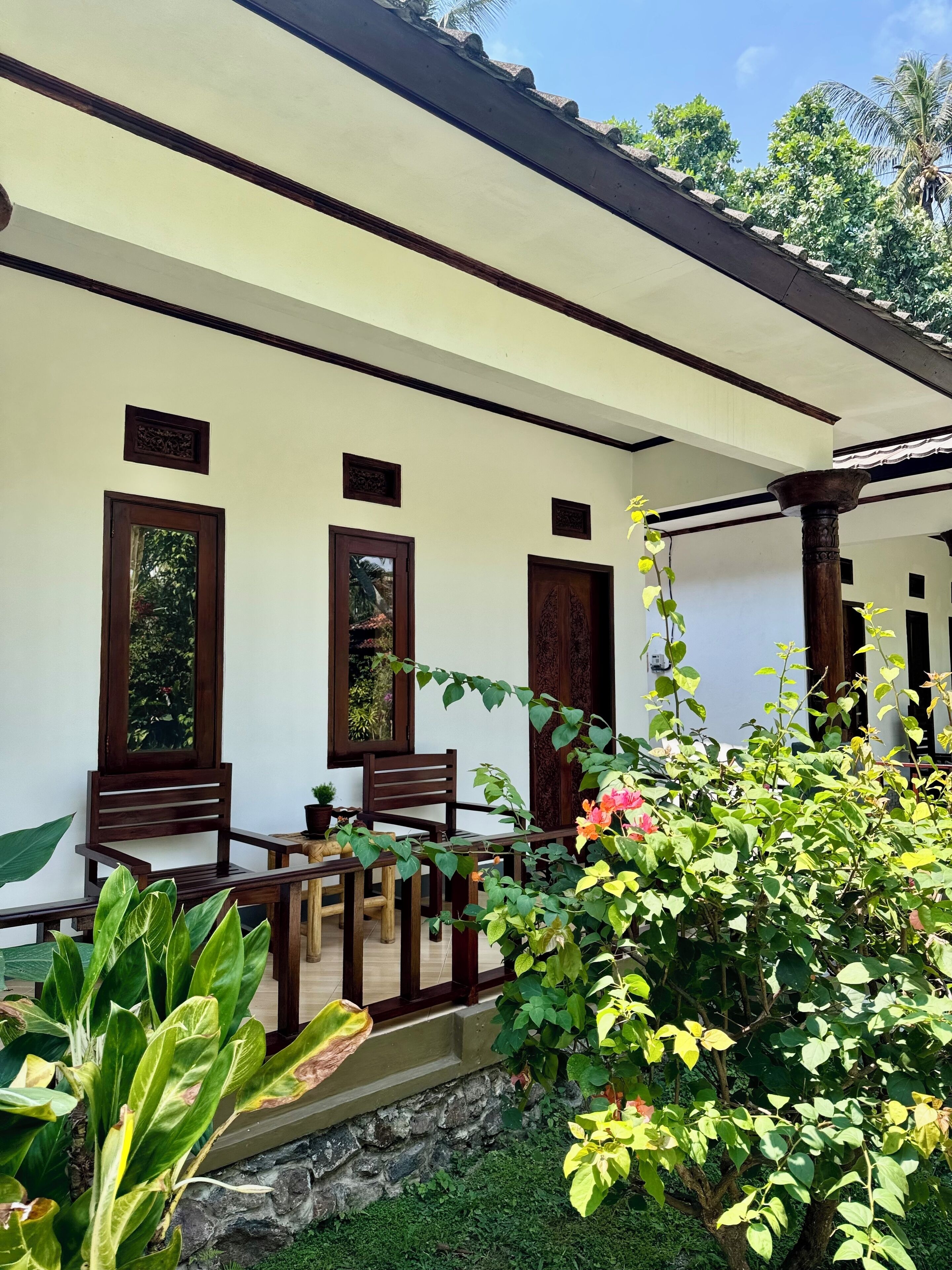 A traditional building with a covered porch, wooden chairs, and potted plants.