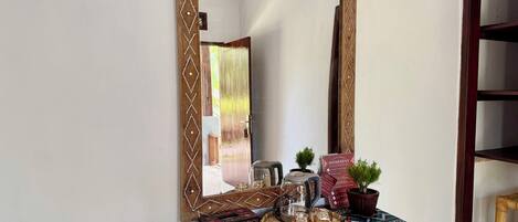 A wooden-framed mirror with a decorative border, a wooden console table with a woven mat, a remote control, a small potted plant, a box, and a glass teapot.