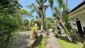 Un chemin de jardin bordé de palmiers, un mur de pierre et un bâtiment avec un toit en tuiles.