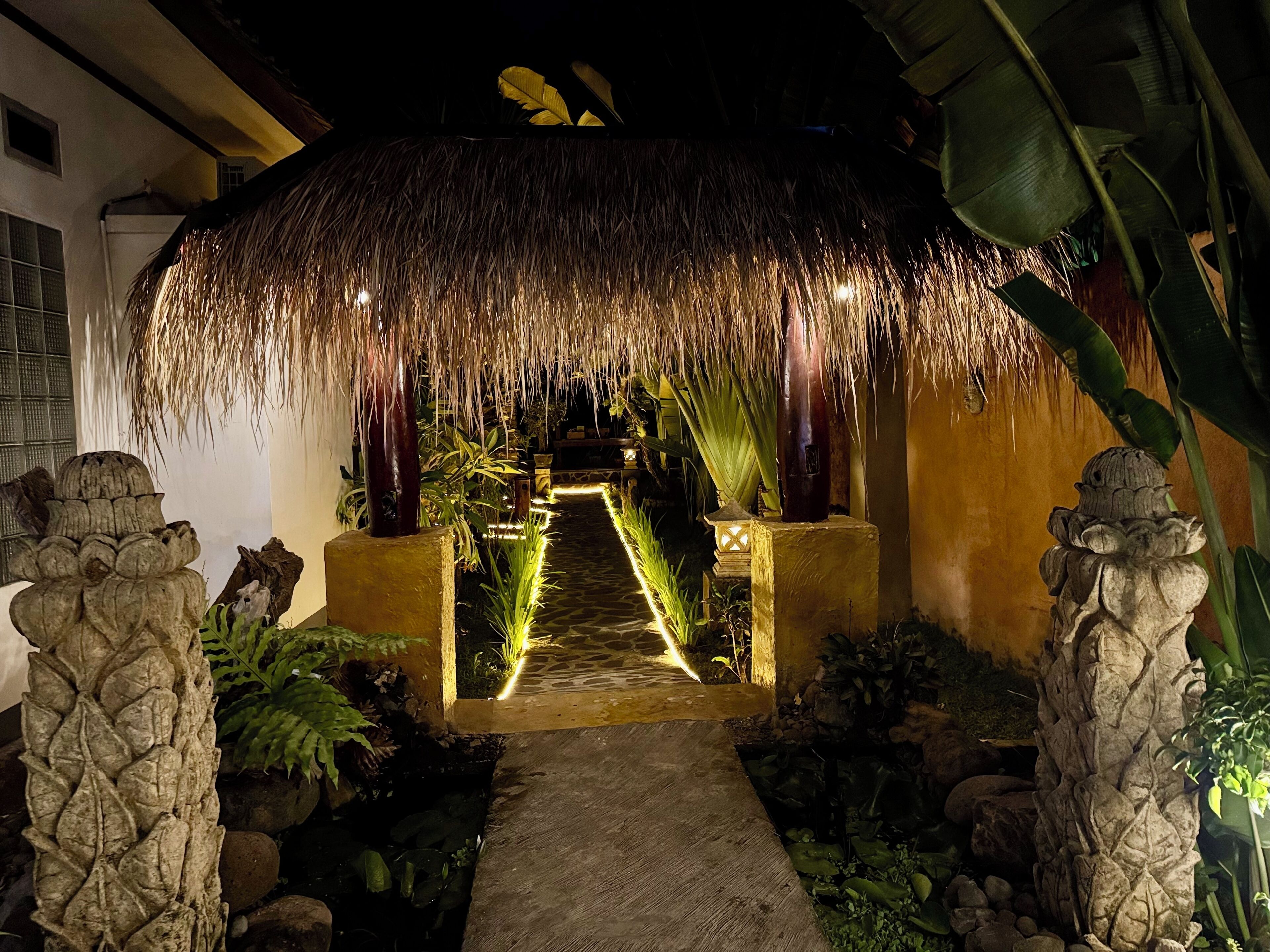 A pathway leading to a thatched-roof structure with a stone pathway and tropical plants.