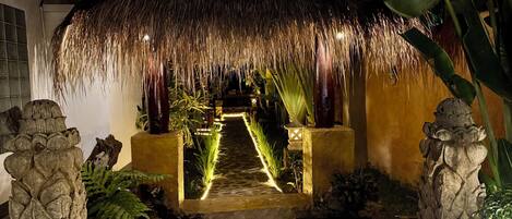 A pathway leading to a thatched-roof structure with a stone pathway and tropical plants.