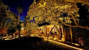 Une vue nocturne d’un hôtel doté d’un jardin bien éclairé, d’un chemin menant à l’entrée et d’un bâtiment au style architectural traditionnel.
