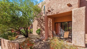 A patio with a table and chairs, surrounded by a garden with red flowers and a tree. - Lux gated condo in Sabino Cyn, relax, explore & create memories 4ever. Book now! (Tucson)