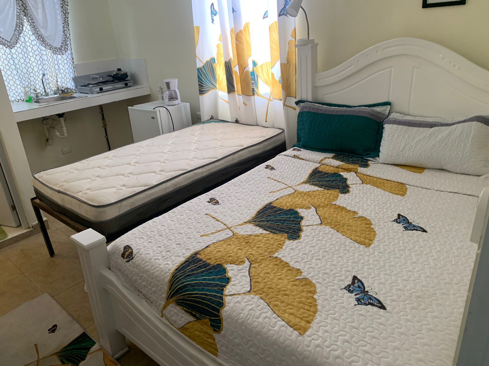 Un dormitorio con cama, una mesita de noche pequeña y una ventana con cortinas.