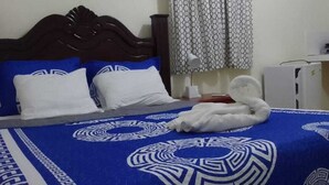 Una habitación de hotel con cama, cabecera de madera, colcha azul estampada, almohadas blancas y una toalla blanca sobre la cama.