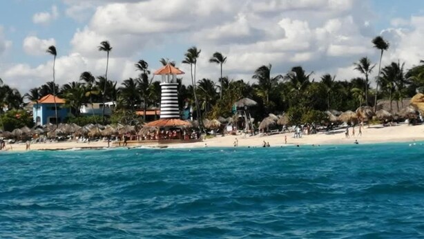 Una playa con una torre rayada, palmeras y una cabaña.