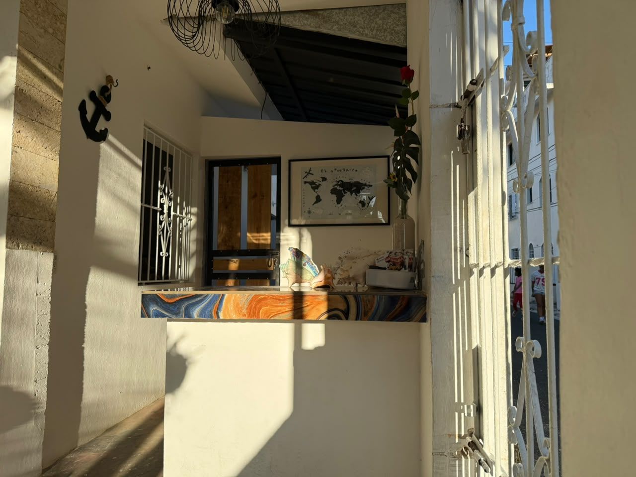 Un couloir étroit, avec une fenêtre sur la gauche, une porte sur la droite et une petite table sur laquelle est posé un vase de fleurs.