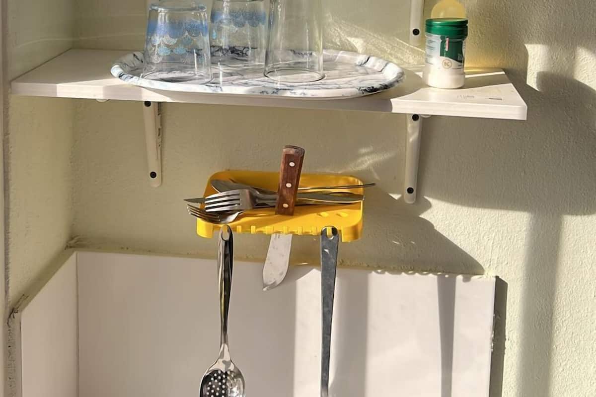 A kitchen shelf with plates, cups, glasses, and utensils.