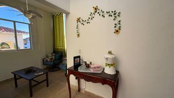 A room with a ceiling fan, a window with a view, a table with a decorative item, and a wall with a floral arrangement.