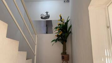 A staircase with a patterned floor leading to a landing. A potted plant with yellow flowers is placed on a small stand.