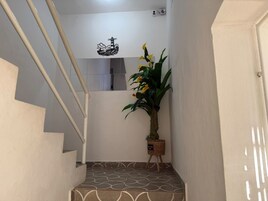 Eine Treppe mit einem gemusterten Boden führt zu einer Zwischenebene. Eine Topfpflanze mit gelben Blüten steht auf einem kleinen Tisch.