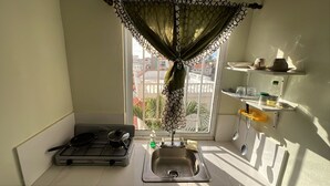 Una cocina pequeña con cocina a gas, un lavamanos y una ventana que ofrece vistas a edificios.