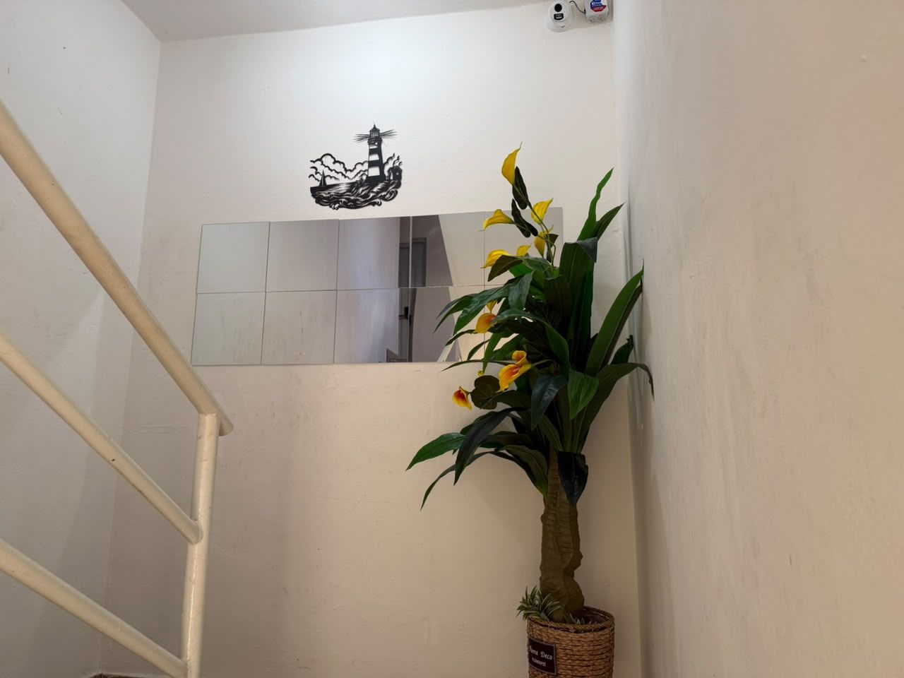 Un escalier avec une rampe blanche, un pot de fleurs contenant des fleurs jaunes et un interrupteur fixé au mur.