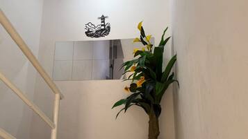 Un escalier avec une rampe blanche, un pot de fleurs contenant des fleurs jaunes et un interrupteur fixé au mur.
