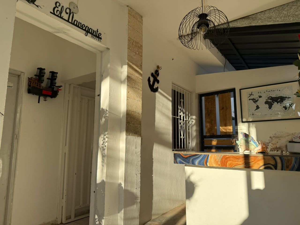 A hotel entrance with a sign reading 'El Navegante Hotel,' a fan on the ceiling, and a window with a view.