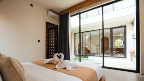 A hotel room with a large bed, a sliding glass door to a balcony, and a view of the outdoor area.