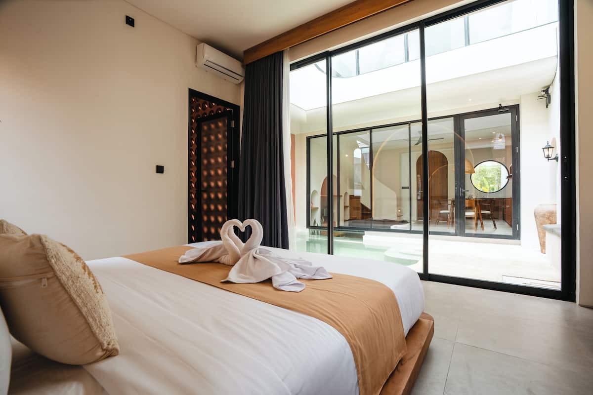 A hotel room with a large bed, a sliding glass door to a balcony, and a view of the outdoor area.