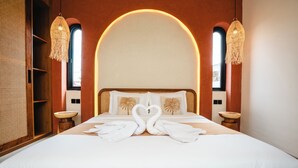 A hotel room with a large bed, two bedside tables, a wooden wardrobe, and a large arched window.