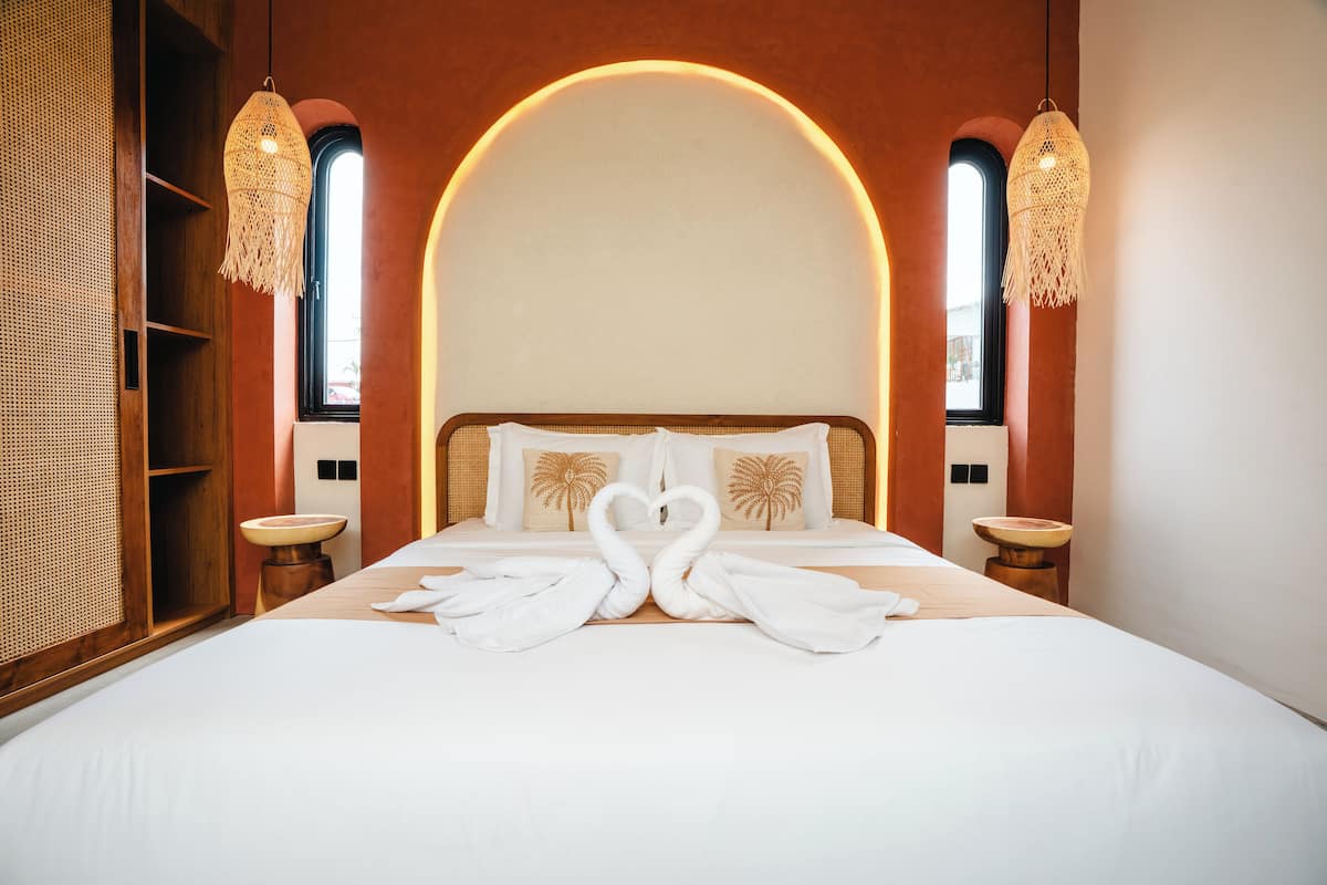 A hotel room with a large bed, two bedside tables, a wooden wardrobe, and a large arched window.