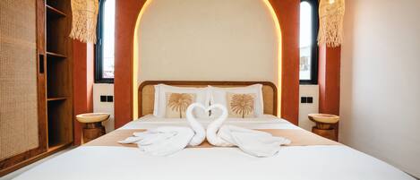 A hotel room with a large bed, two bedside tables, a wooden wardrobe, and a large arched window.