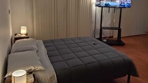 Een hotelkamer met een groot bed, een op een standaard gemonteerde televisie, een nachtkastje met een lamp en een raam met gordijnen.