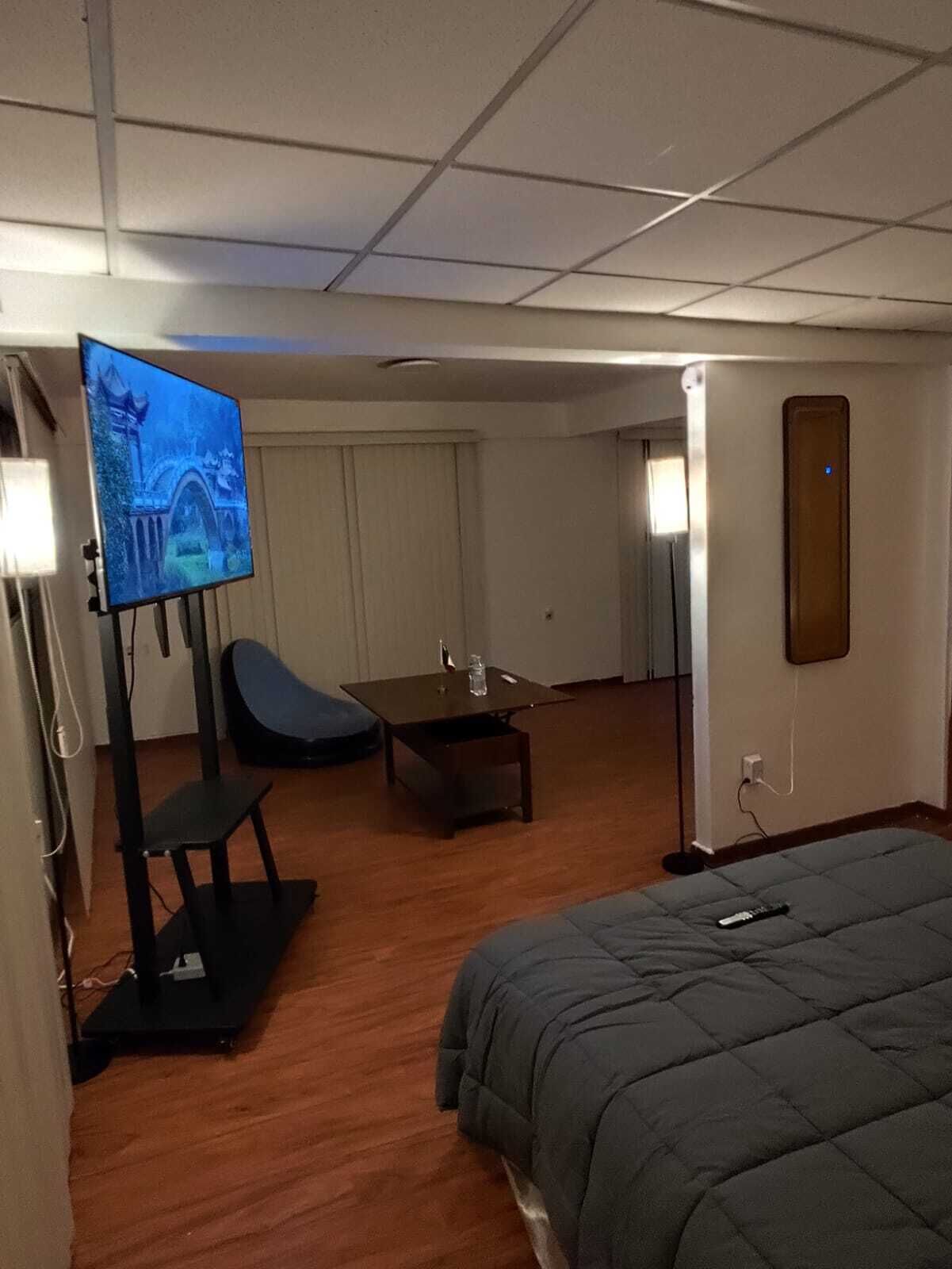 A hotel room with a bed, a TV on a stand, a chair, a small table, and a door leading to another room.