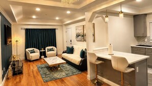 A modern living room with a sofa, two armchairs, a coffee table, and a kitchen area with a bar stool. - Luxurious 3-bedroom 2 bath near NYC train station, EWR. (Newark)