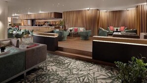 Un moderno vestíbulo de hotel con una zona de estar central, un bar y una cocina al fondo.