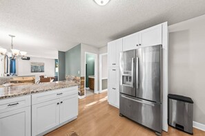A modern kitchen with white cabinets, a stainless steel refrigerator, and a granite countertop. - Space for 10+ and Fenced Yard, The Indigo House! (North Charleston)