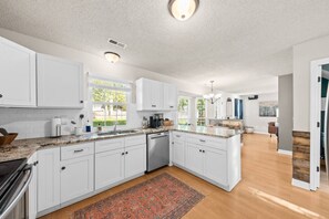 A modern kitchen with white cabinetry, granite countertops, and a central island. - Space for 10+ and Fenced Yard, The Indigo House! (North Charleston)