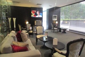 Een moderne hotel lobby met een bank, stoelen, een salontafel en een televisiescherm.
