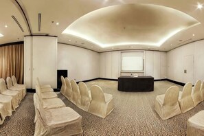 Een vergaderzaal met een gebogen plafond, een groot scherm en rijen stoelen.