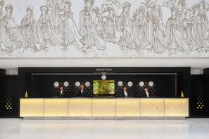 Zona de recepción de un hotel con mostrador de mármol, un escritorio de recepción y un mural en la pared.