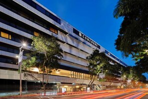 Un hotel de varios pisos con un diseño arquitectónico moderno, destacando una señalización llamativa y una fachada bien iluminada.