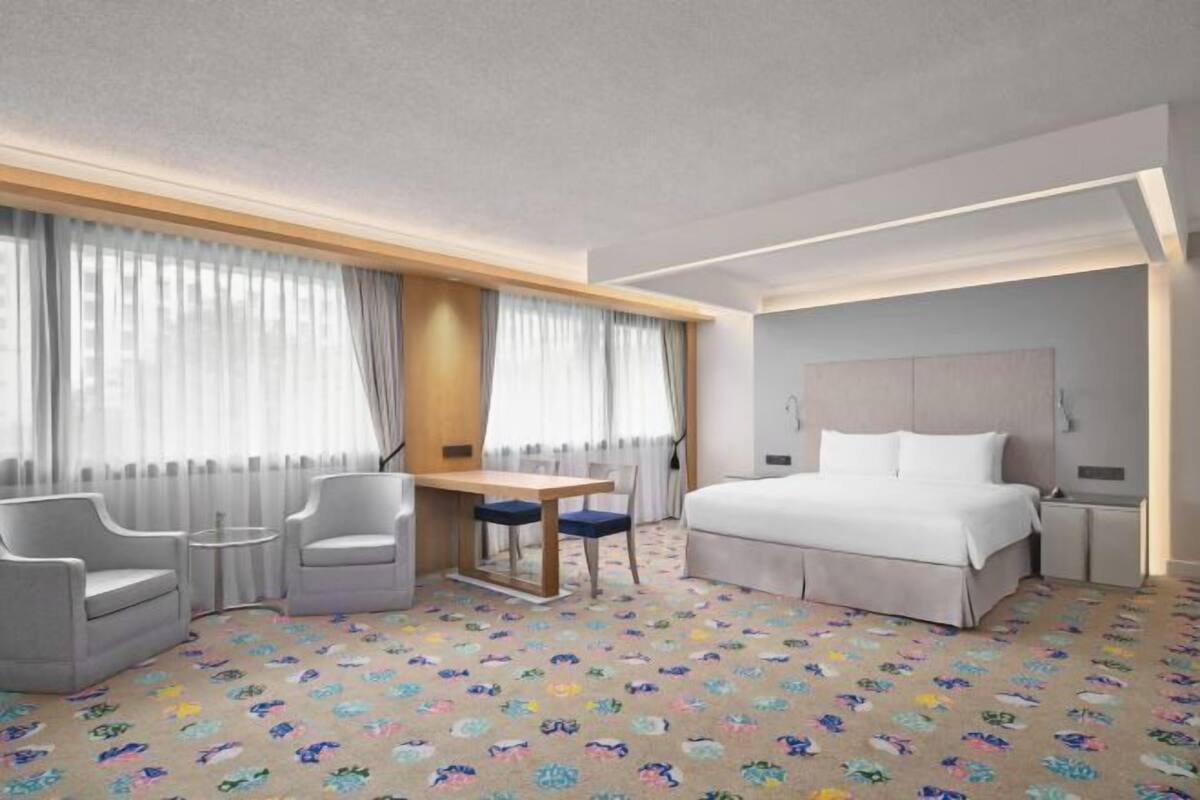 A hotel room with a bed, two chairs, a small table, and a desk.