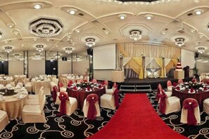 Une salle de banquet avec des tables rondes, un tapis rouge et une scène avec des rideaux.