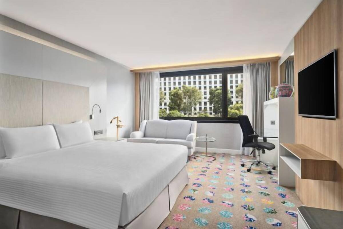 A hotel room with a bed, a sofa, a TV, a small table, and a window with curtains.